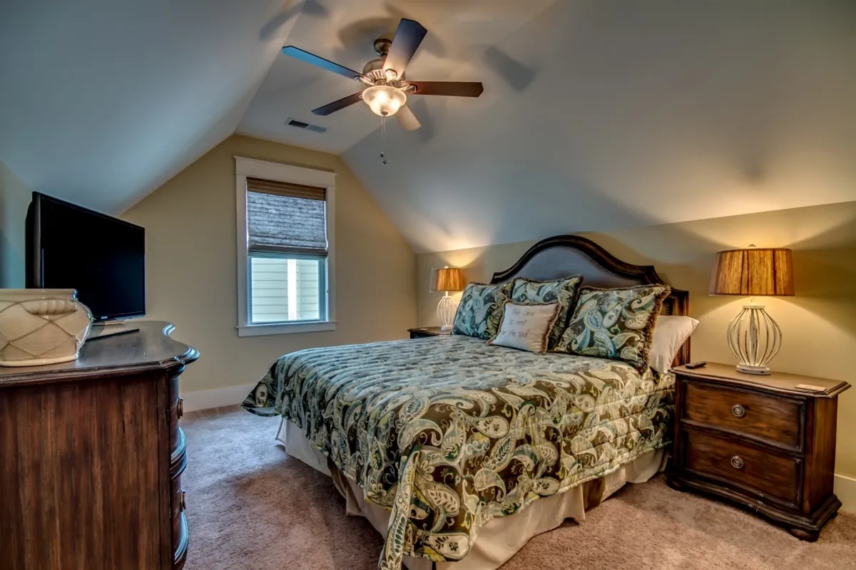 An inviting bedroom featuring a king-sized bed adorned with decorative pillows, flanked by nightstands with lamps and a television opposite the bed. The space is cozy and restful, ideal for quiet evenings or relaxing after a busy day.