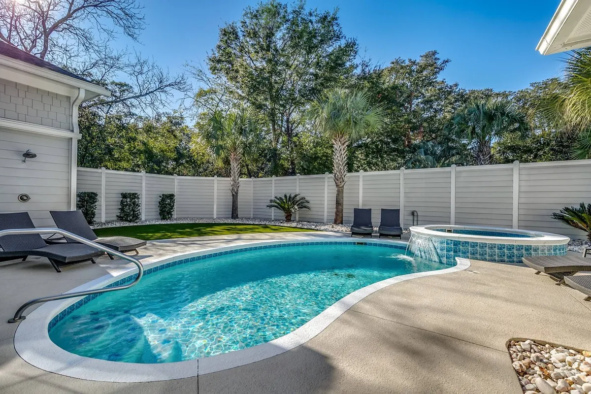 A serene exterior view of a private swimming pool and bubbling hot tub, surrounded by lush palm trees and equipped with inviting lounge chairs. The atmosphere is tranquil with hints of golden sunlight, ideal for both sunbathing and relaxing dips. The pool and hot tub are positioned in a way that suggests privacy and luxurious comfort, with plenty of space for socializing or quiet moments.