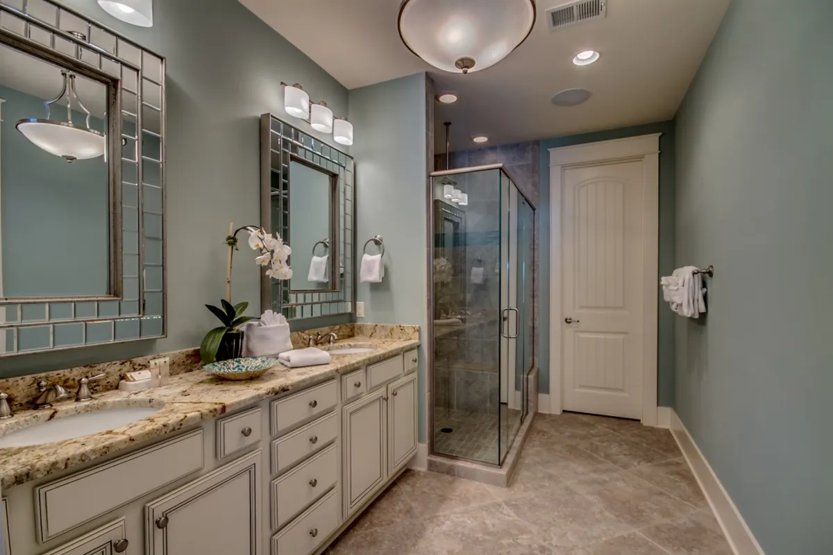 A stylish en-suite bathroom with a mirrored vanity, granite countertop, glass shower enclosure, and a decorative orchid. The calm and refreshing atmosphere evokes a spa-like experience, perfect for post-pool refreshes or daily routines.