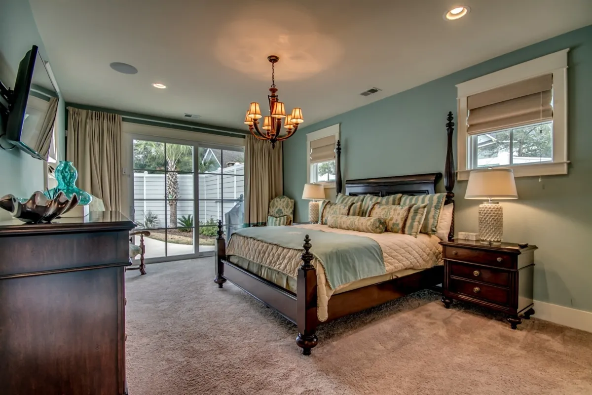 A tranquil bedroom scene featuring a plush king-size bed with a chandelier overhead and a television mounted on the wall. Sliding glass doors open to natural light, offering a serene spot for morning coffee or evening relaxation. The room exudes a sense of privacy and comfort, ideal for restful nights.
