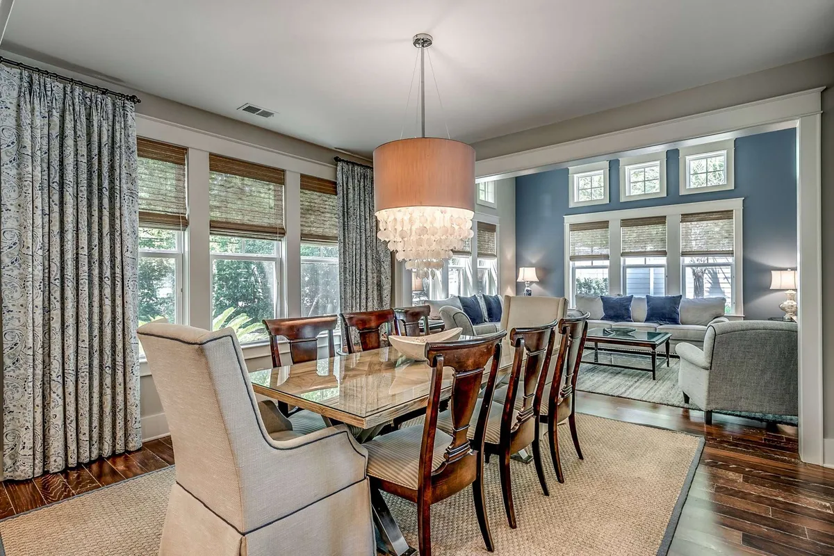 An elegant dining area with a stylish chandelier and large windows, seamlessly connected to the adjacent living space. The dining table is set for gatherings, supporting both formal dinners and casual family meals, with plenty of natural light creating a warm, welcoming mood.