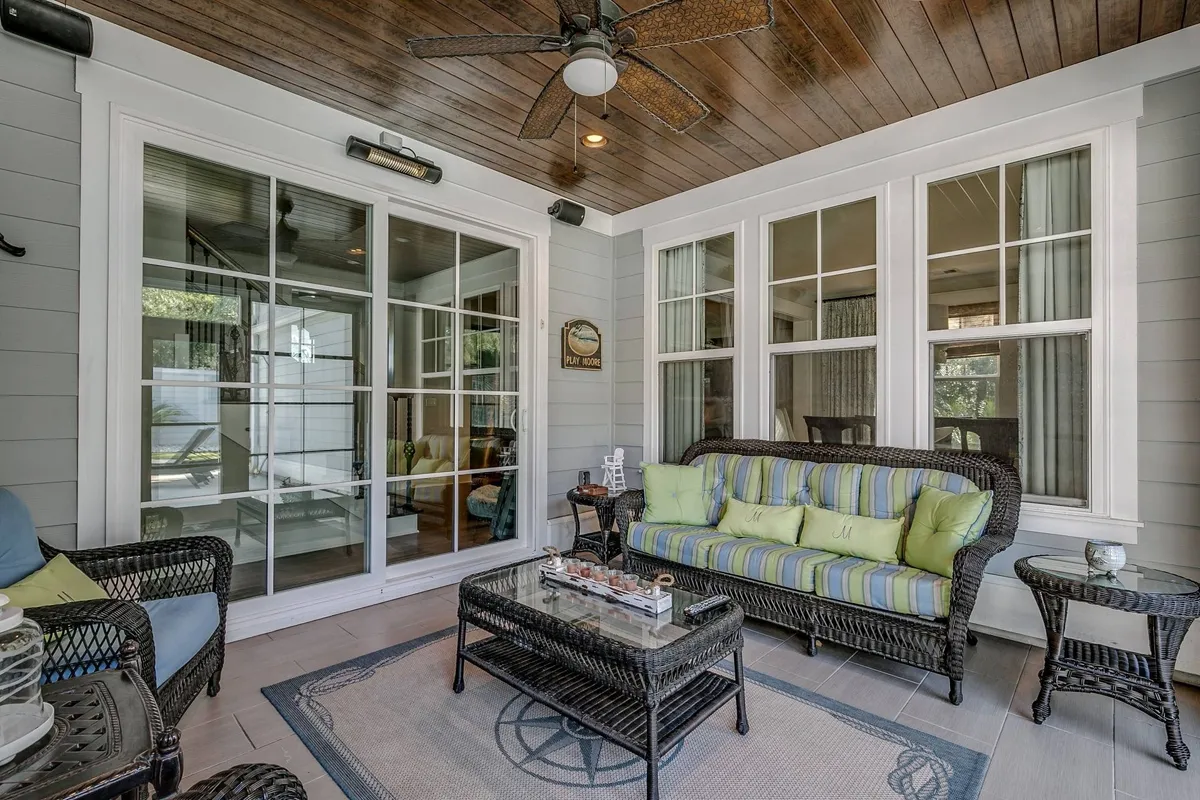 A sunroom furnished with a comfortable wicker sofa and a glass coffee table, bordered by expansive windows that let in abundant natural light. The tranquil setting is perfect for enjoying morning coffee, reading, or transitioning into a screened porch for breezy evenings or movie nights.